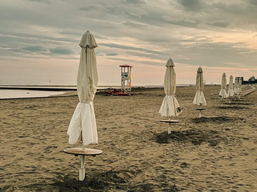 Closed beach umbrellas in a row, lifeguard tower in the distance