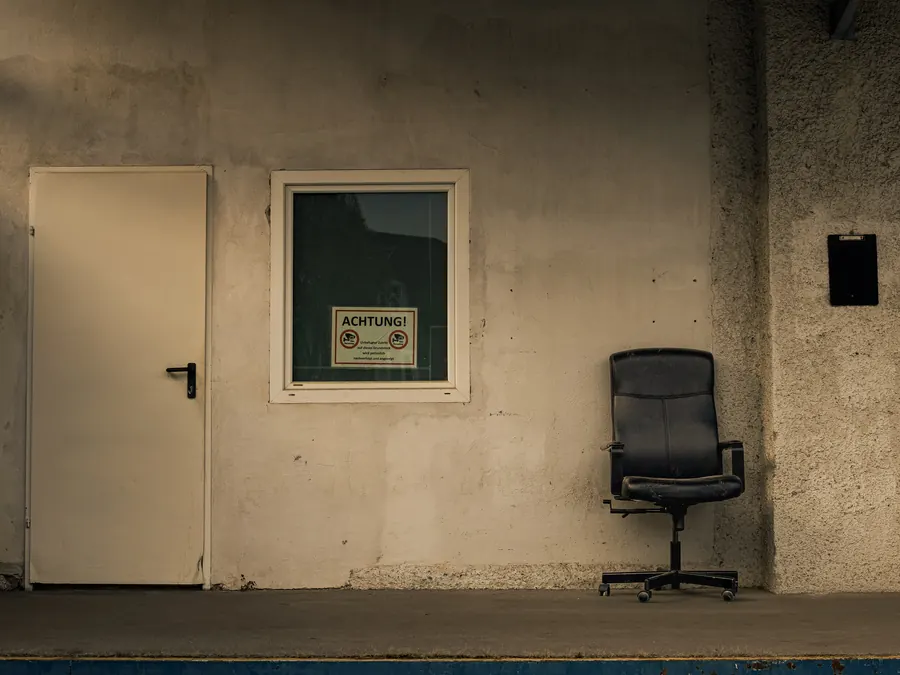 Black office chair in front of a concrete wall with a warning sign