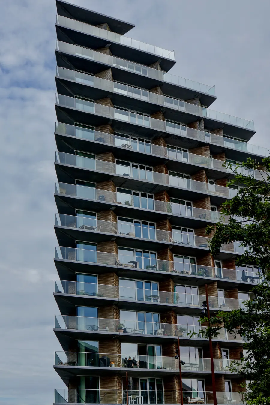 Tapering residential tower with stacked glass balconies against a cloudy sky