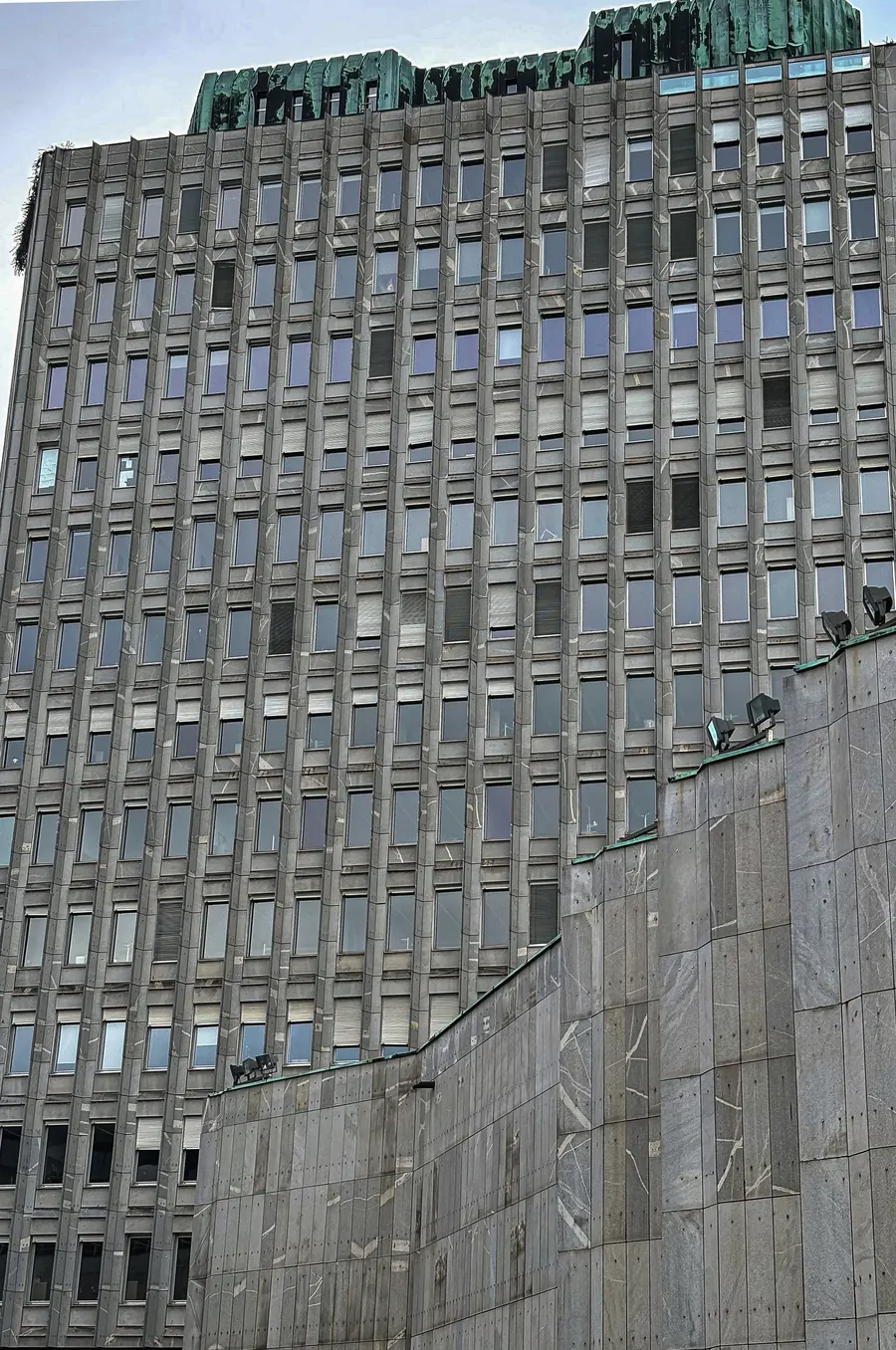 Concrete wall rising diagonally across a gridded tower facade