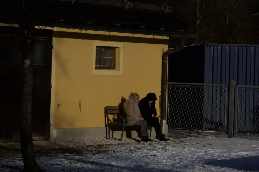 Two people on a bench outside a yellow house at night, snow on the ground