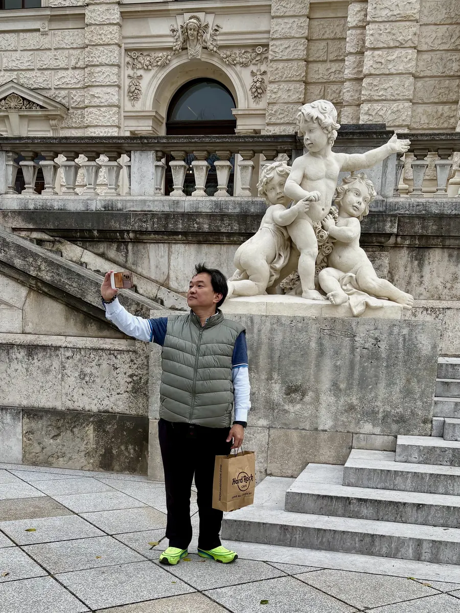 Man taking a selfie in front of a baroque statue of putti