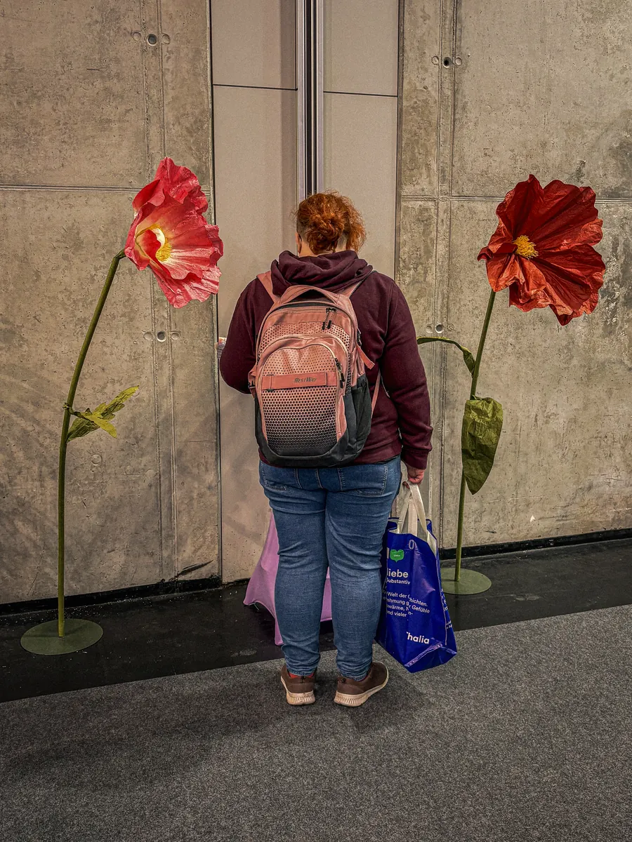 Woman with a backpack standing between two giant paper flowers