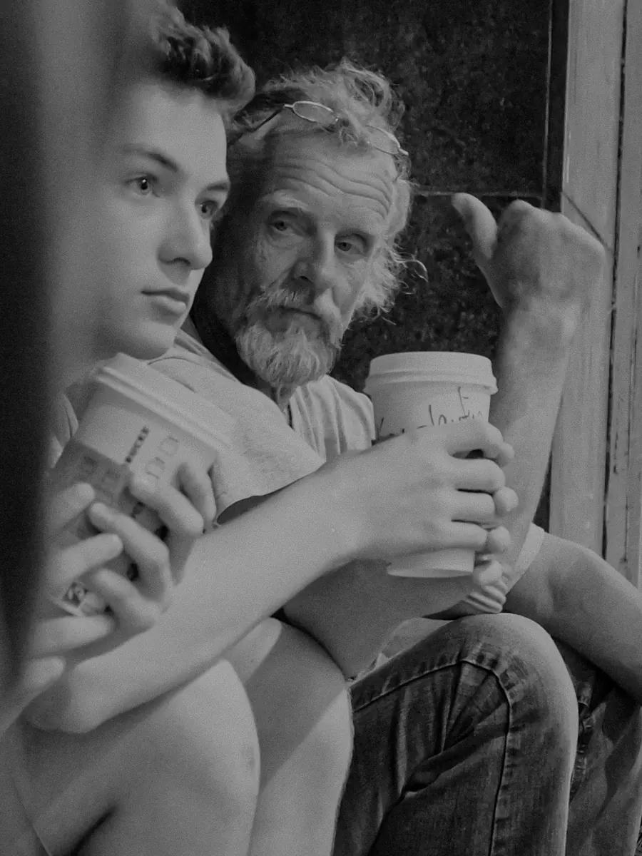 Young man and old bearded man sharing coffee in a doorway