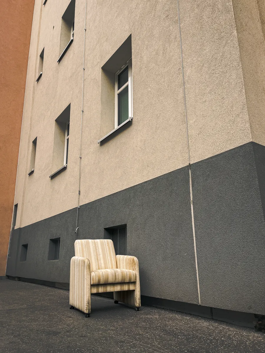 Striped armchair left on the pavement against a building wall