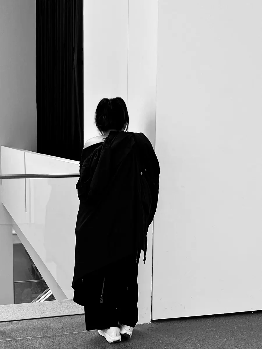 Woman in a long black coat in a white museum space