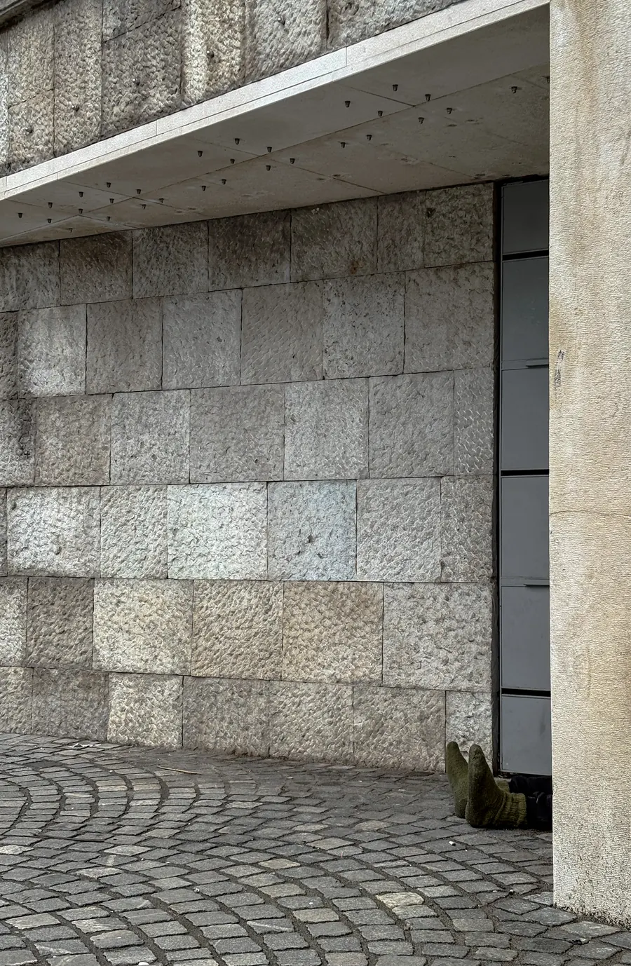 Two feet in green socks protruding from a doorway beside a massive stone wall