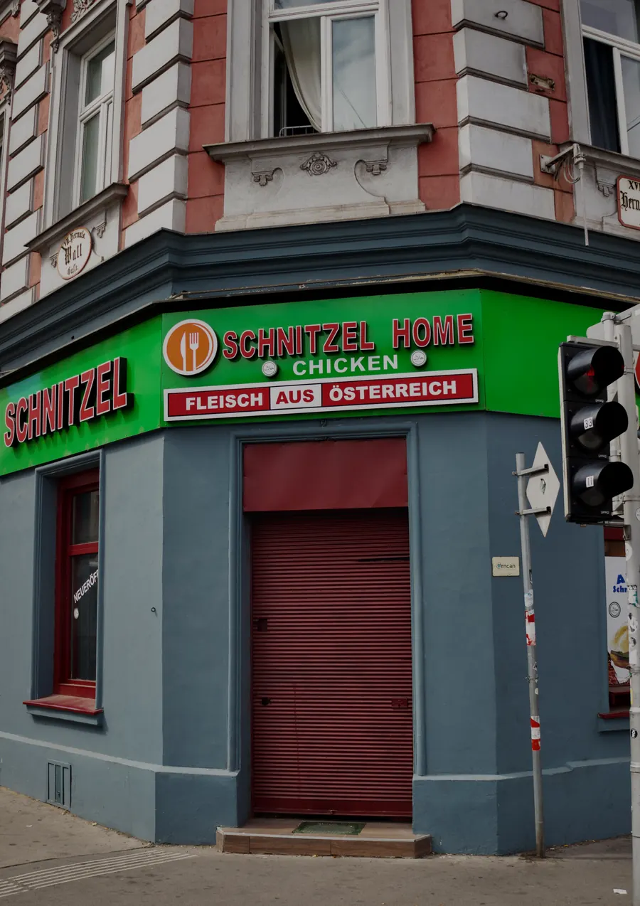 Closed corner shop with a green Schnitzel sign and a red door, Vienna