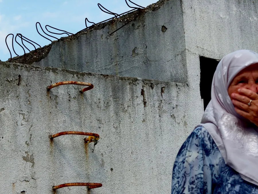 Woman covering her mouth beside a concrete wall with barbed wire, Potočari
