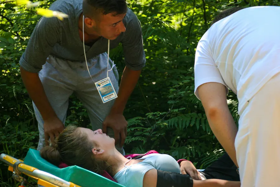 A young participant bends over an exhausted marcher lying on a stretcher in the forest