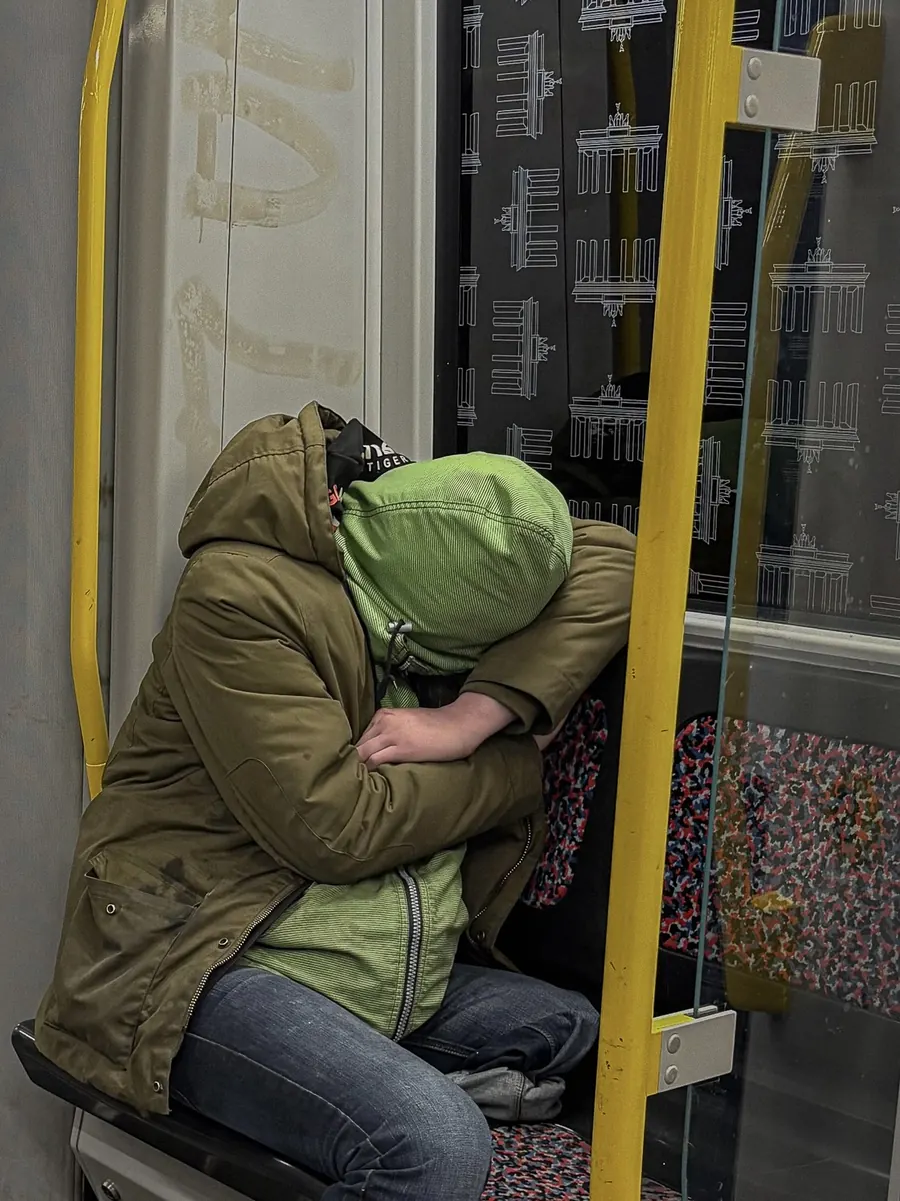 Figure folded over in a green hood on a Berlin U-Bahn seat, face hidden