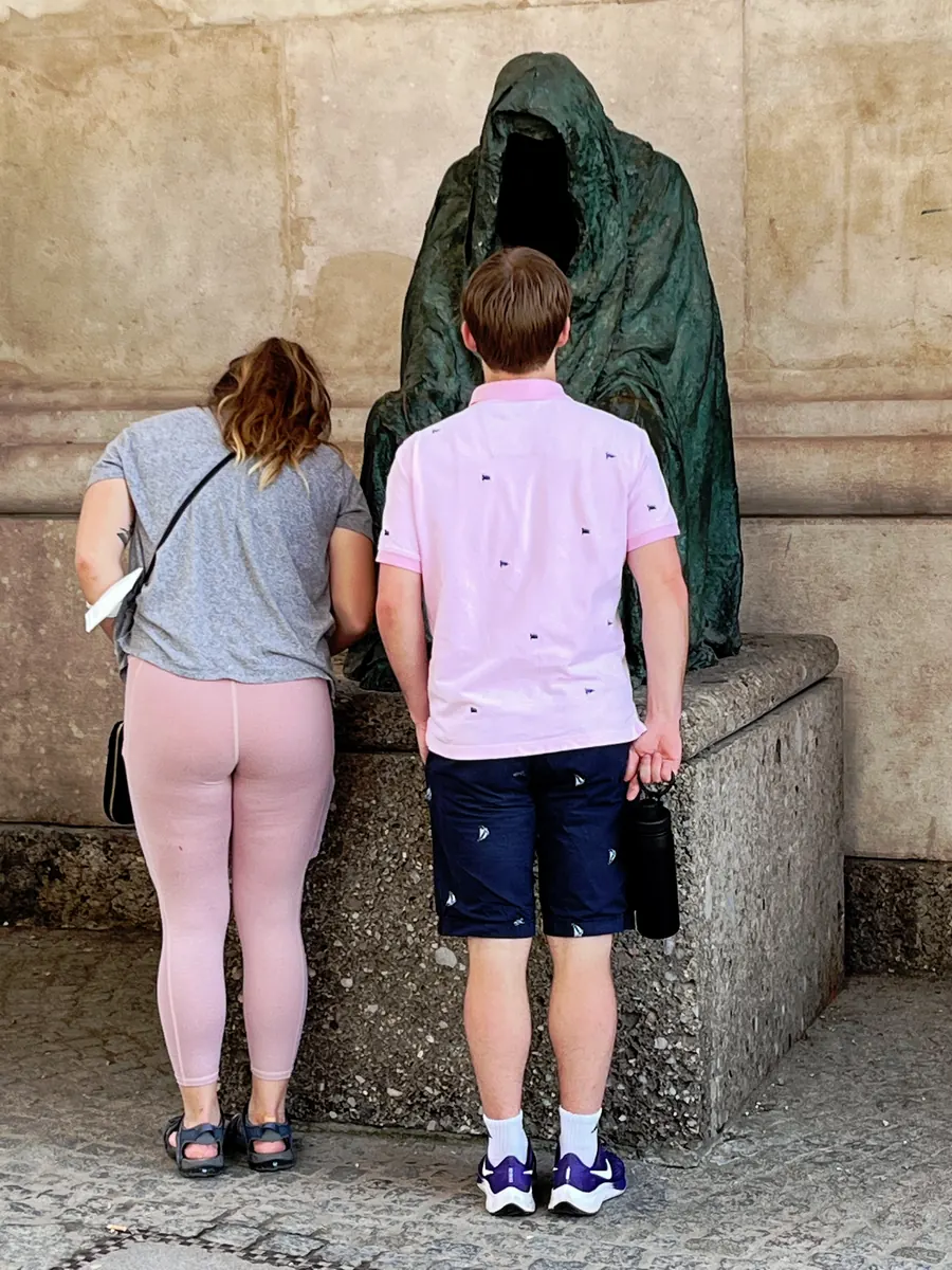Tourist couple examining a hooded bronze figure