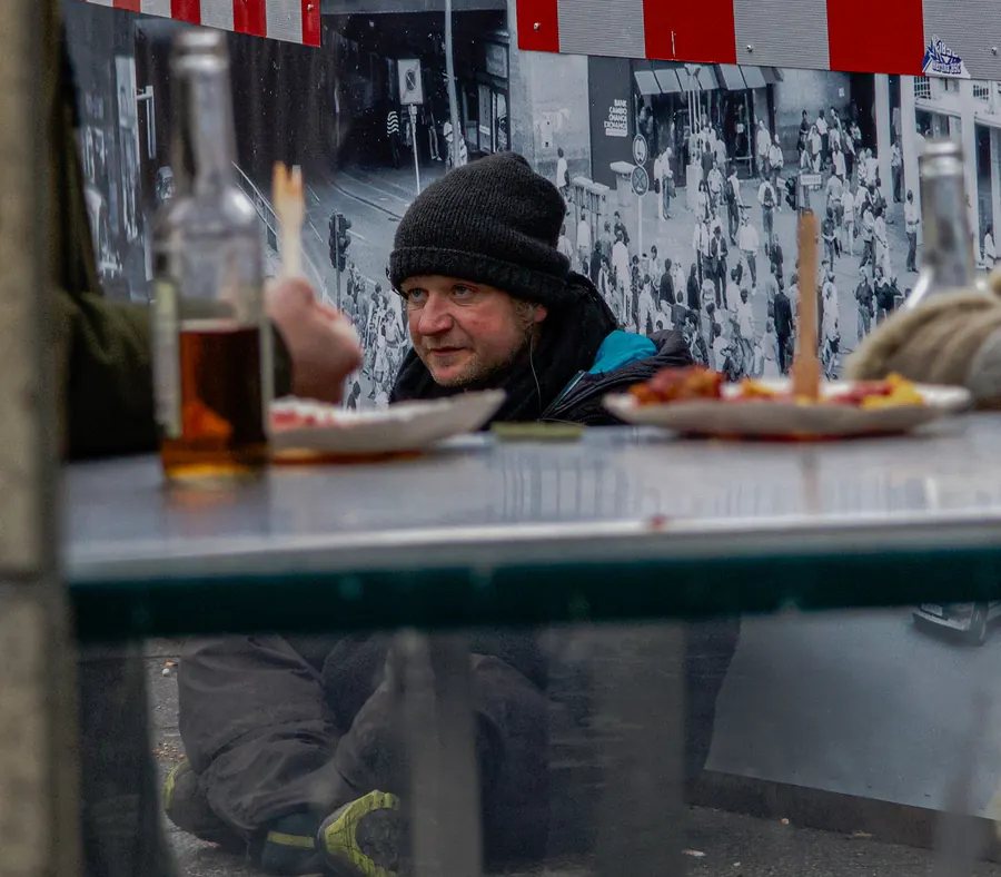 Man in a black beanie behind bottles at a street food stand