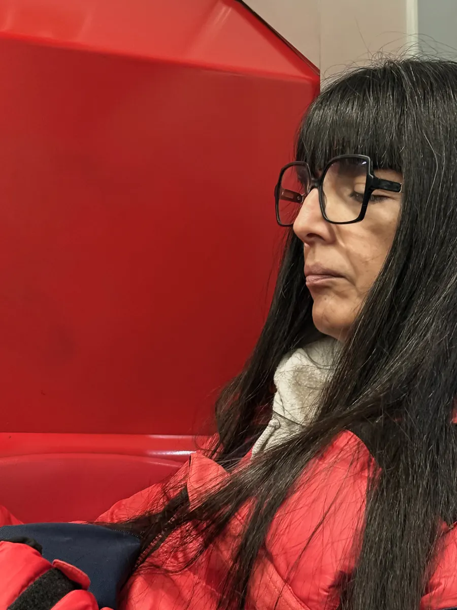 Woman with black fringe and glasses against a red wall