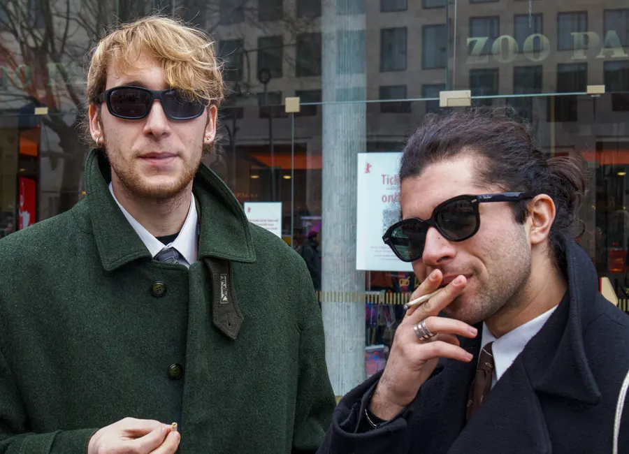 Two young men in sunglasses and coats, one smoking