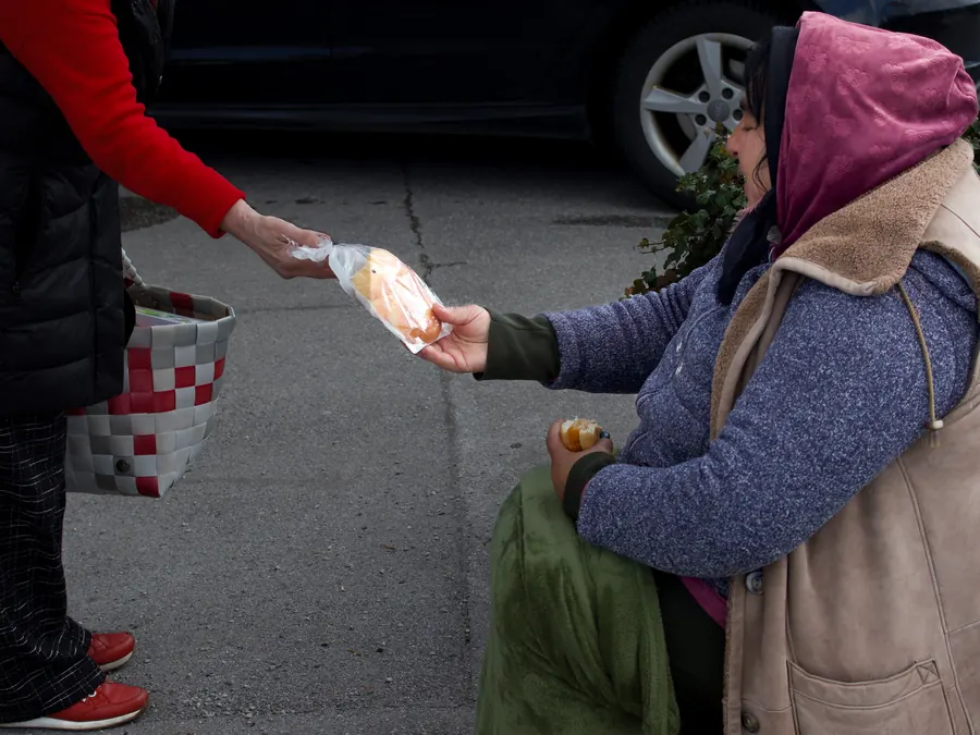 Someone handing a bag of bread to a seated woman