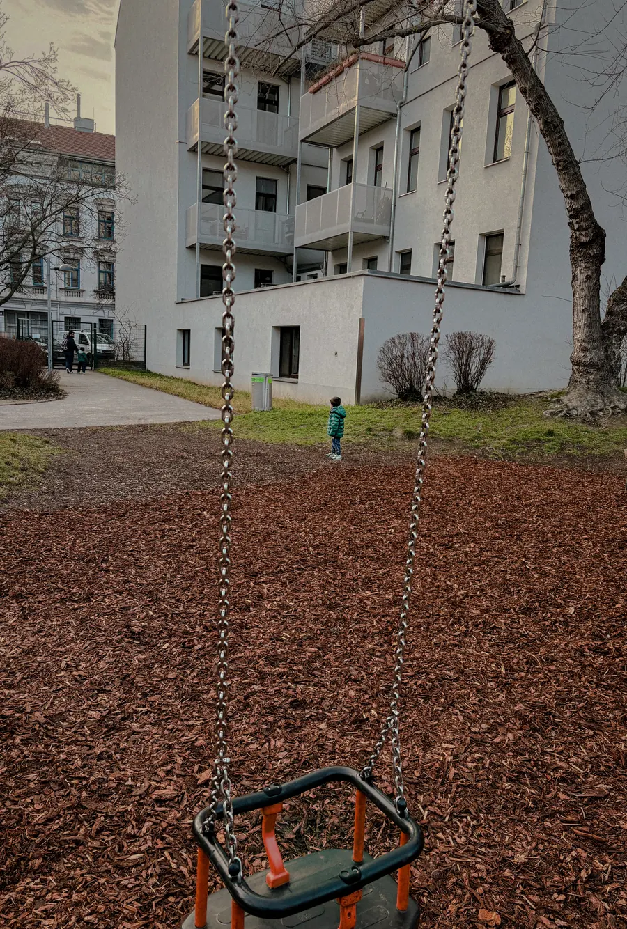 Empty swing seat hanging over bark mulch between apartment blocks