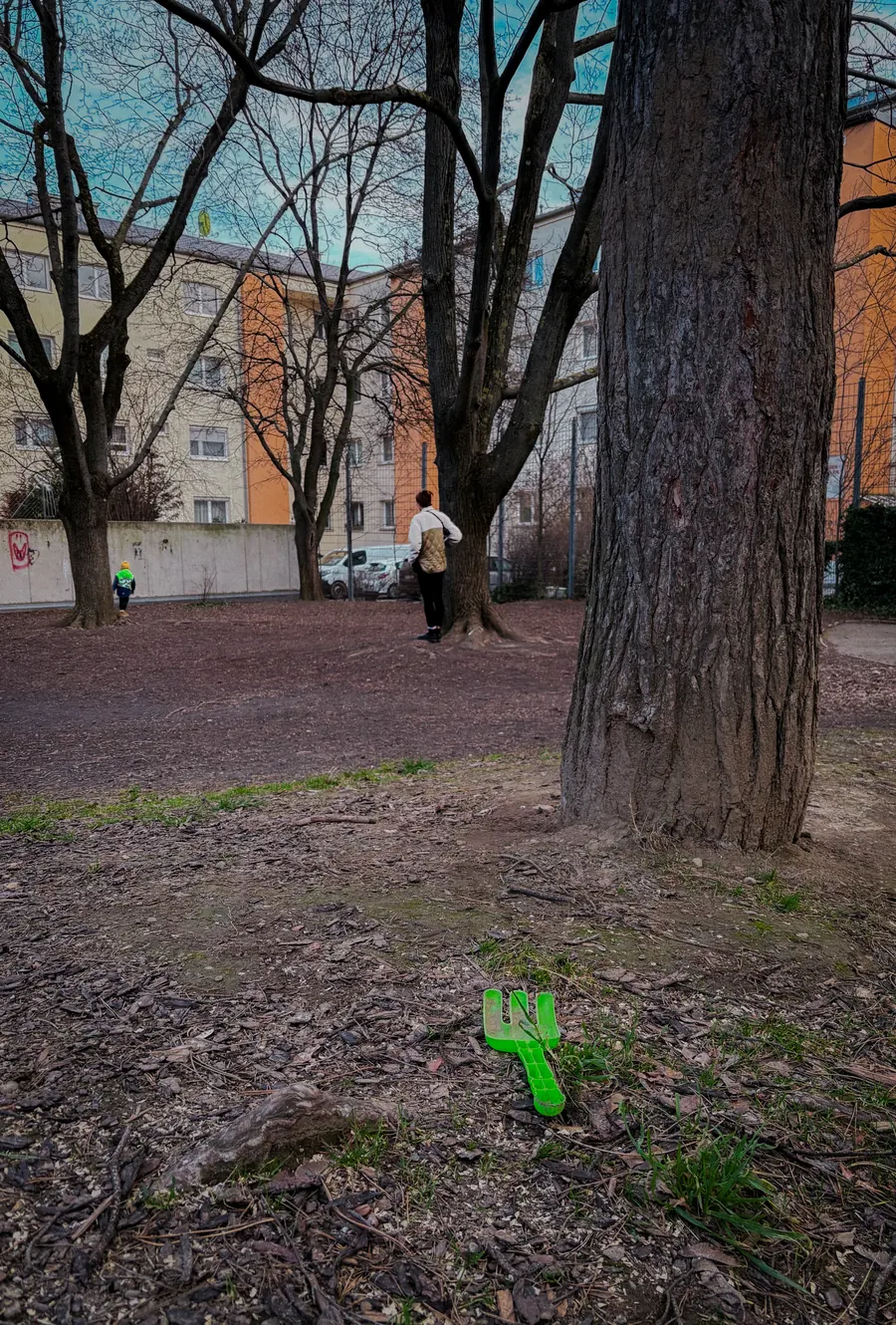 Green toy shovel left in the dirt beneath a large tree