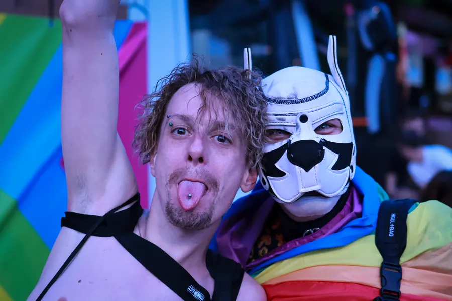Man sticking out his tongue beside a friend in a white animal mask at Pride