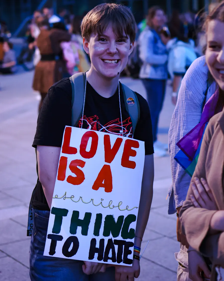 Smiling young person wearing a sign reading Love is a terrible thing to hate
