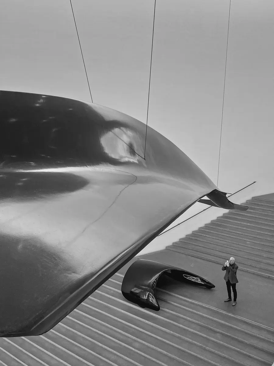 Large dark sculpture above a museum staircase, a tiny visitor below