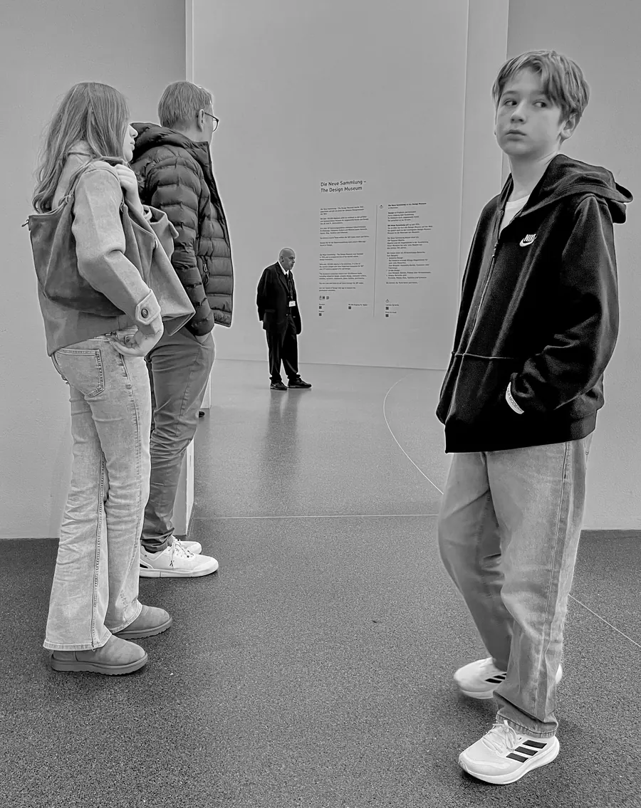 Teenager looking back in a white gallery hall, a guard in the distance