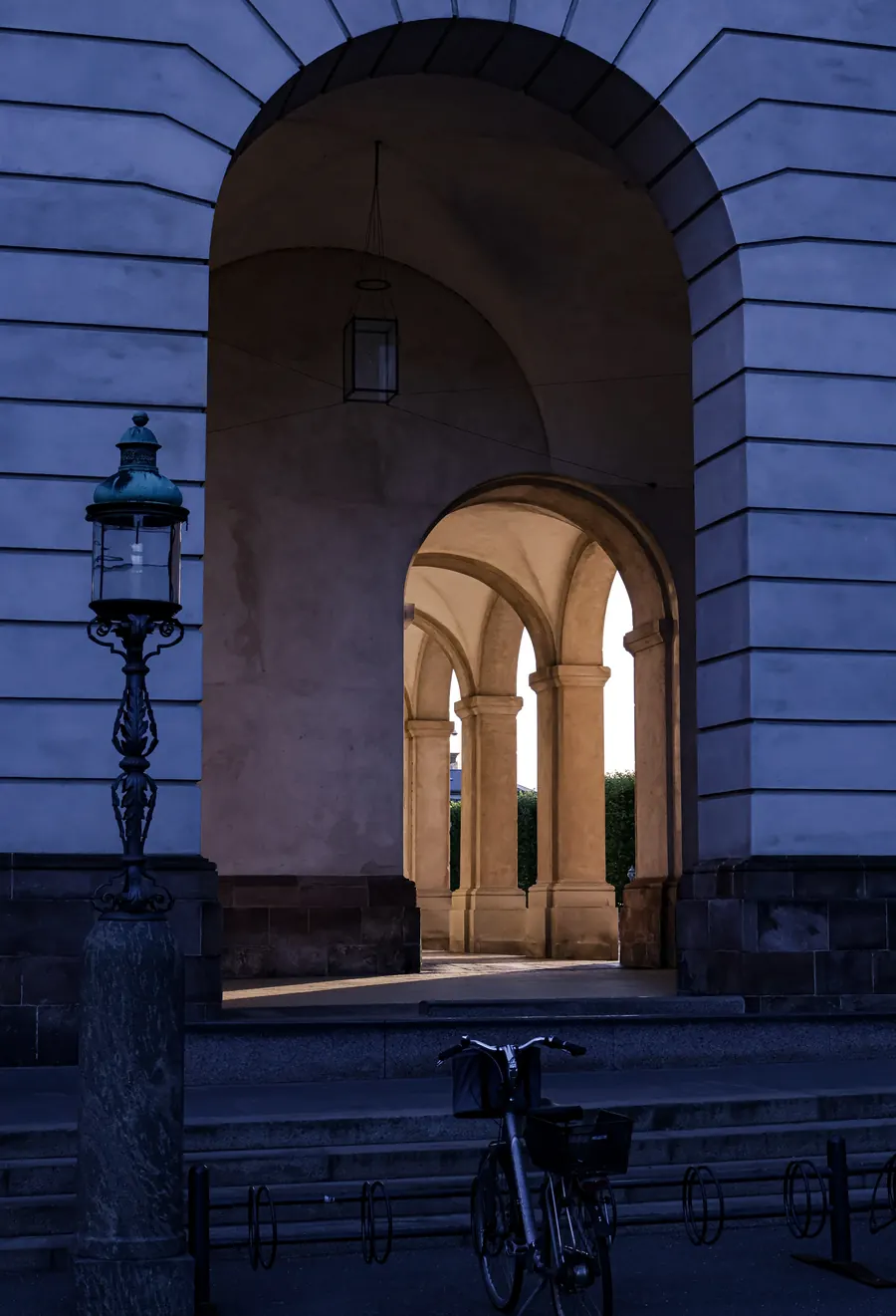 Arched passage with a lantern and bicycle, warm light on columns beyond