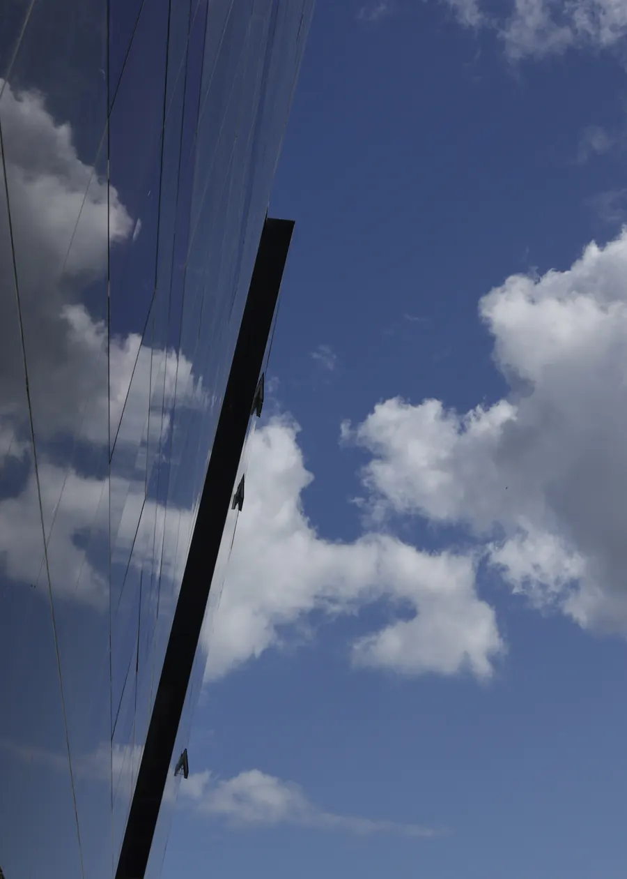 Dark glass facade reflecting clouds and blue sky